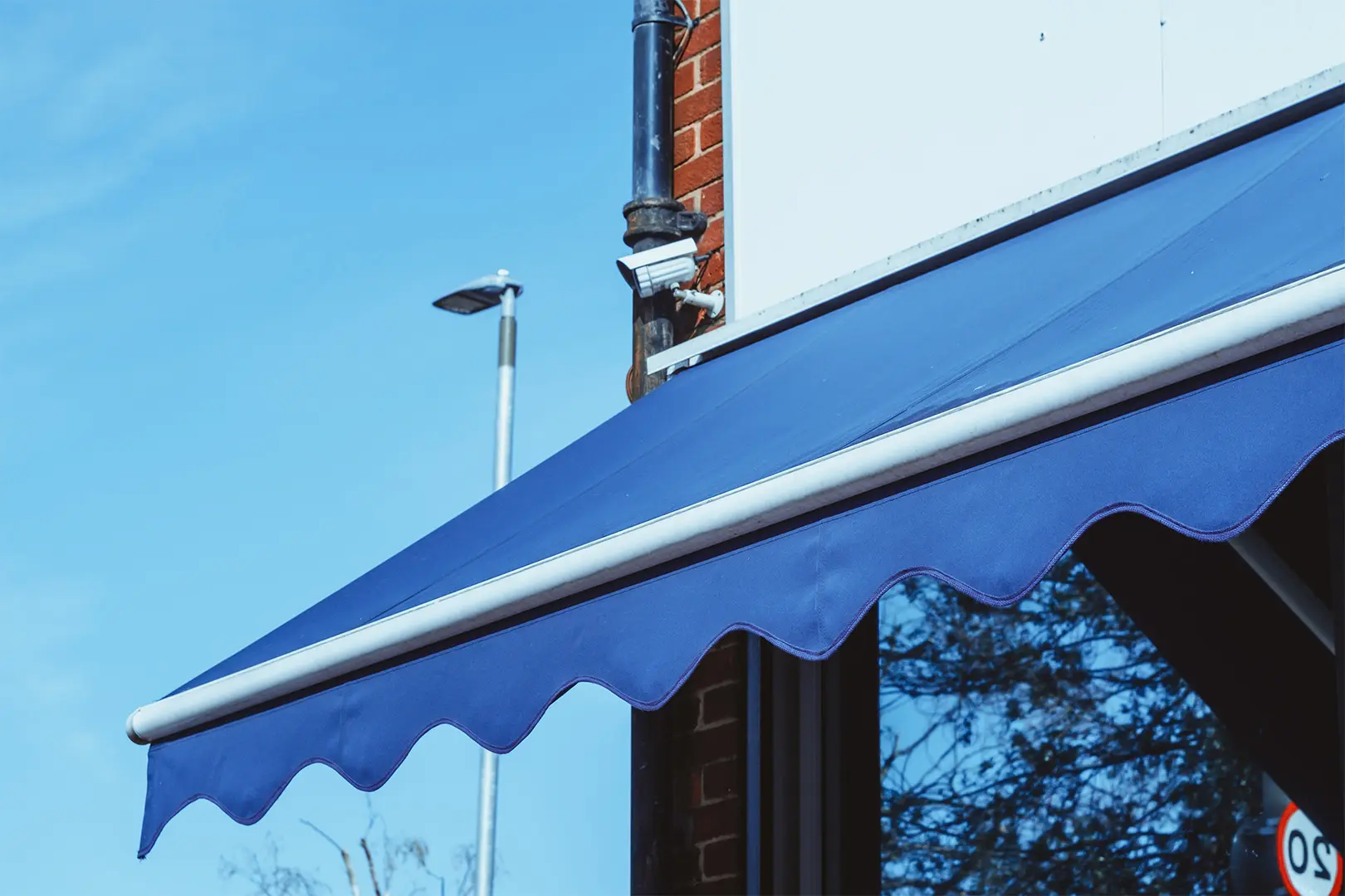 A blue awning with a scalloped valance against a clear sky